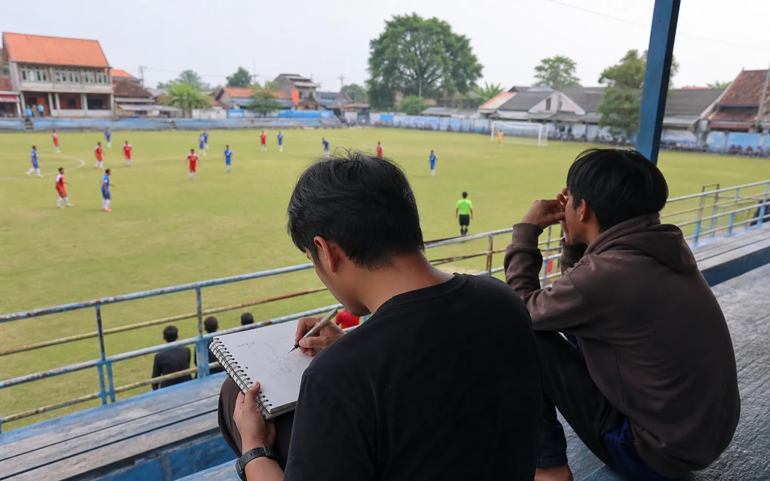 Dua penonton mempelajari pergerakan pemain dari tribun lokal yang terbuka