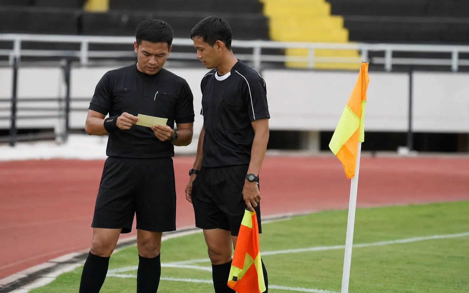 Ofisial dan asisten meninjau lembar pola pergerakan tanpa tulisan di dekat bendera sudut